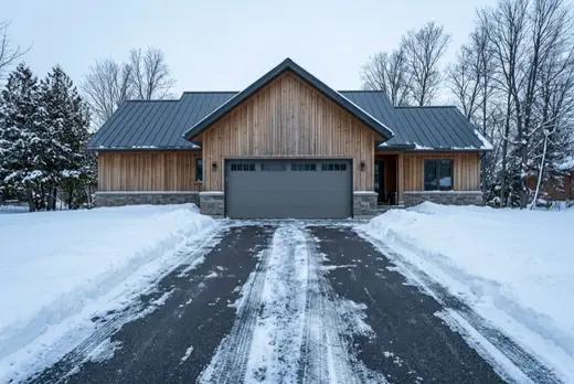 A plowed driveway running up to the closed garage door of a timber chalet, snowbanks pushed clear to either side